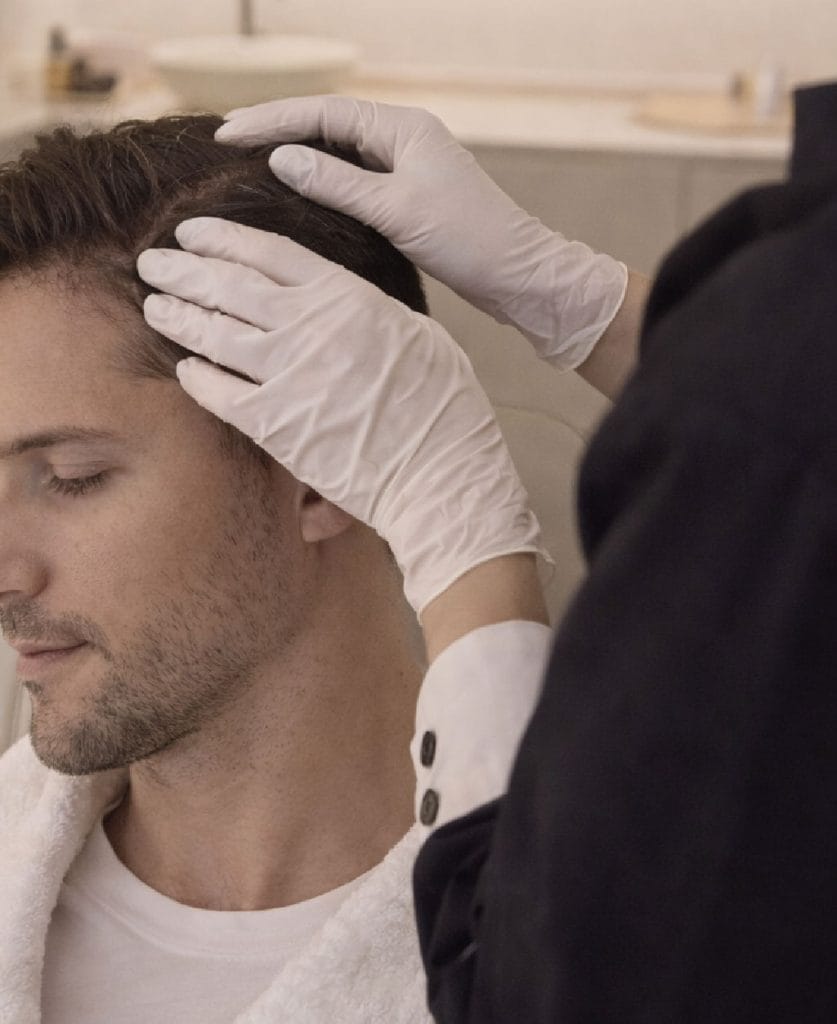 Médica especialista evaluando cuero cabelludo de paciente masculino en consulta de medicina capilar en Valencia.